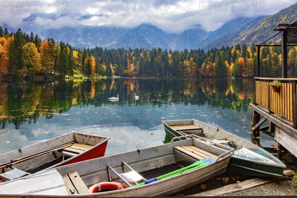 The boat dock. The Lago Fusine in Italy. The bright colors of the autumn forests are reflected in the icy water of the lake. Mountains covered in morning mist