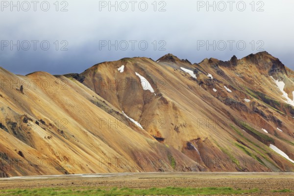 Smooth orange rhyolite mountains in Landmannalaugar nature reserve. In the hollows snow left over from last year