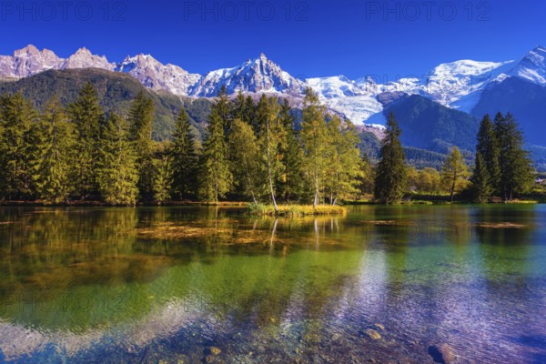 The snow-covered Alps and evergreen fir-trees are reflected in lake. Early fall in Chamonix, Haute-Savoie. France