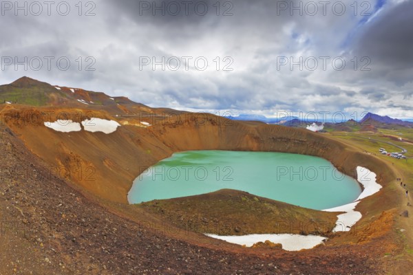 July in Iceland. Lake in the crater of an extinct volcano. Lake water bright green color. On the shores lie snowfields from last year