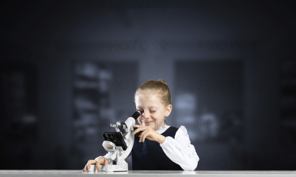 Little girl scientist looking through microscope in classroom at biology lesson. Research and discovery. Formal education in modern school. Schoolgirl in schoolwear making experiment in class