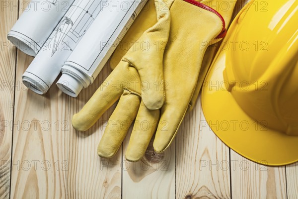 Blueprints yellow gloves and construction helmet on wood boards