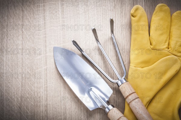 Stainless gardening trowel fork with hand spade and leather safety gloves on wooden board agriculture concept