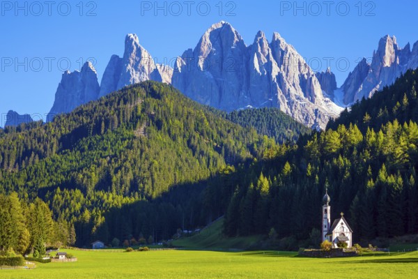 Small white church with among green lawns on the sunset. The village Santa Maddalena in the Val di Funes Valley. Italy, Tyrol. The concept of active, ecological and photo tourism