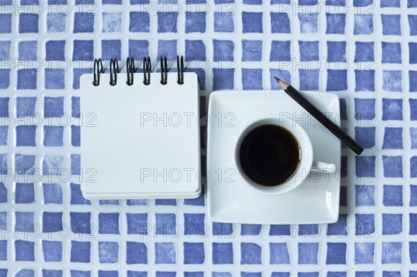 Blank white notepad and cup of coffee on blue ceramic mosaic table. top view, copy space