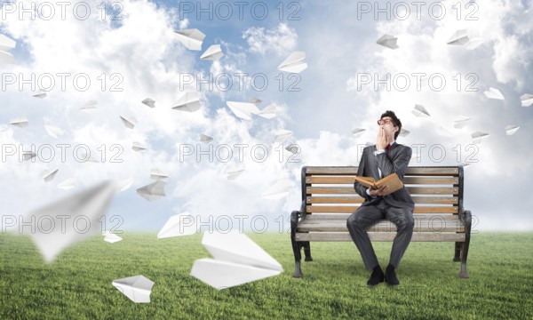 Young student with a book on the bench. traditional learning concept. paper planes fly around