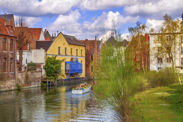 Ghent, Belgium, April 12, 2016: Old houses along canal and boat with tourists in popular touristic destination Gent