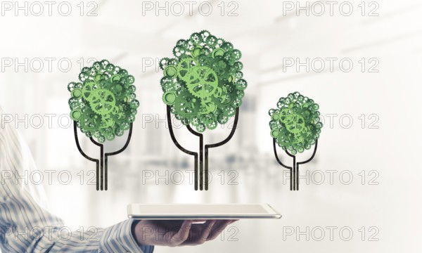 Close of businessman holding tablet pc with green tree made of gears and cogwheels. Mixed media