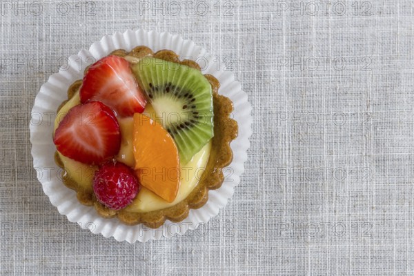 A cake with cream and mixed fruit, resting on linen tablecloth
