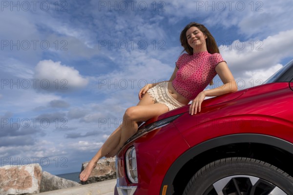 A gorgeous redhead model sits confidently on the hood of her car, soaking in the summer breeze as she embarks on an exciting cross-country adventure, the open road stretching ahead with endless possibilities, Milwaukee, United States of America