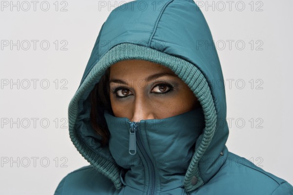 A young woman wearing a green winter coat using the hood to cover her head so that only her eyes are visible, isolated on white, New York, USA