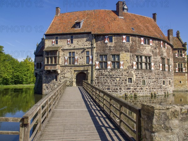 Historic castle with striking wooden bridge and tiled roof, surrounded by moat and blue sky, vischering, lüdinghausen, germany