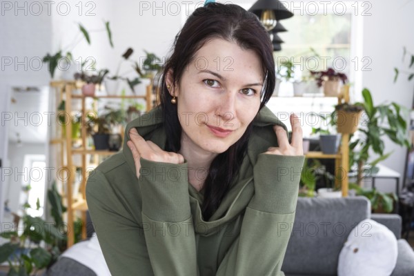Large portrait Joyful emotions of a woman in the hood in her home in a bright modern interior with home plants. Eco-friendly portrait with real joy