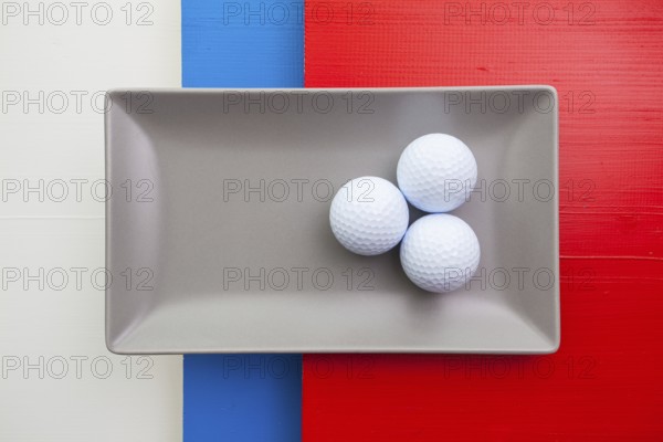 Gray ceramic dish with golf equipments on over white, blue and red wooden table, rectangle dish