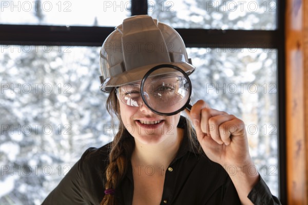 Caucasian worker woman smiling. construction inspector looking through a magnifying glass. she wearing grey hardhat during home air quality inspection