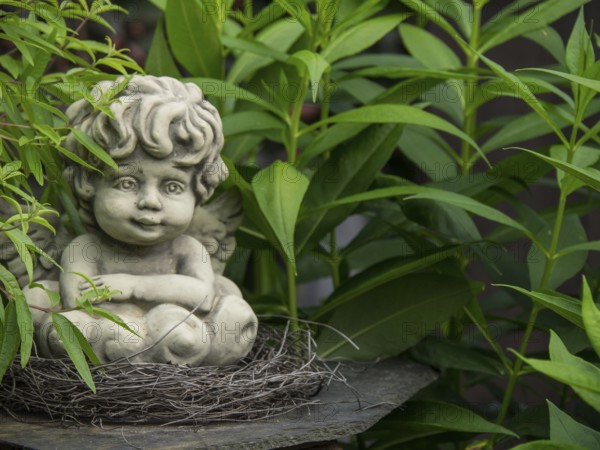 Angel figure made of stone embedded in a nest, surrounded by green plants, borken, münsterland, germany