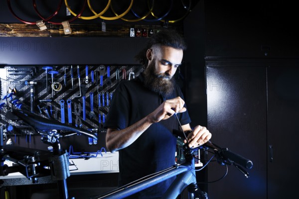 Theme sale and repair of bicycles. Young and stylish with a beard and long hair, a Caucasian man uses a tool to set up and repair a bike in a store. Business owner at work