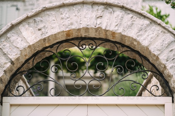 Arched metal forged lattice in a stone fence. Close-up.