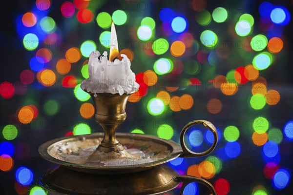 Glowing old candle in wintage candlestick on surface of mirror with multycolored bokeh horizontal version