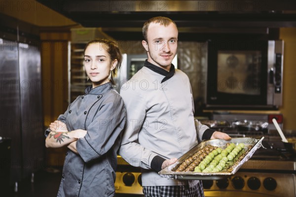 Profession preparation confectionery products. Caucasian man and woman two employees colleague teamwork pastry chef posing looking camera in uniform in kitchen holding sweets dessert candy truffle