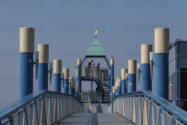 Blue jetty with yellow elements, modern architecture, blue sky, some people on the platform, norden, norddeich, north sea, germany