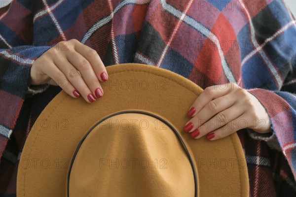 Stylish red female nails. Woman in poncho holding brown trendy hat. Modern Beautiful manicure. Autumn winter nail design concept of beauty treatment. Gel nails. Skin care. Wellness. Trendy colors