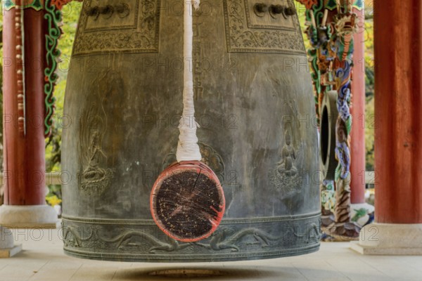 Closeup of bronze bell and striker in pavilion in mountainside Buddhist temple