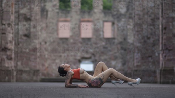 Woman in sporty pose and high heels lying on the ground in front of an old ruin, Staged outdoor shooting, Mindelheim, Unterallgäu, Bavaria, Germany