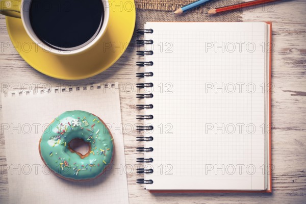 Opened notepad and cup of coffee with donut on wooden table