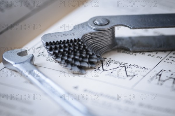 Detailed view of a fanned-out thread gauge with a small spanner lying next to it on an old technical drawing