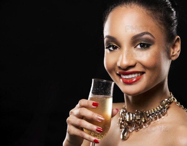 Romantic Indian woman with golden makeup and nailpolish. Big gold fashion necklace. Black isolated background. Holding glass of champagne, Toronto, Canada