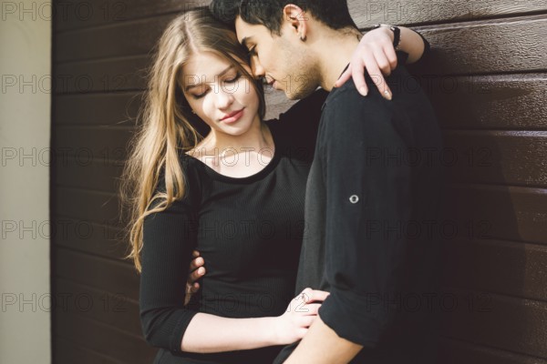 Portrait of attractive Mixed-race couple standing together against the background of a wooden wall. Dating, multiethnic wearing black clothes. Stylish young couple is spending time together outdoors