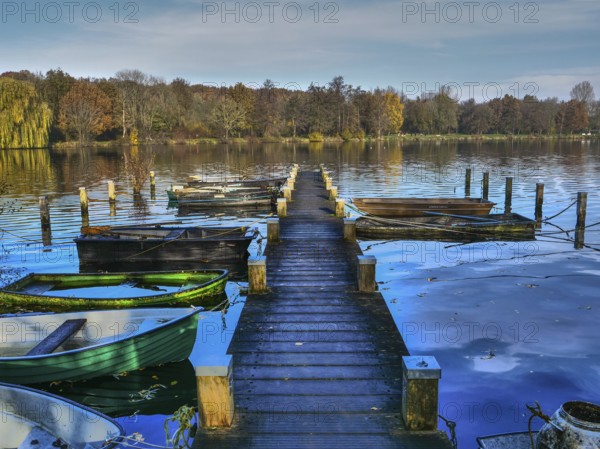 Wooden jetty leading to several boats on a lake with autumn landscape and blue sky, Borken, münsterland, germany