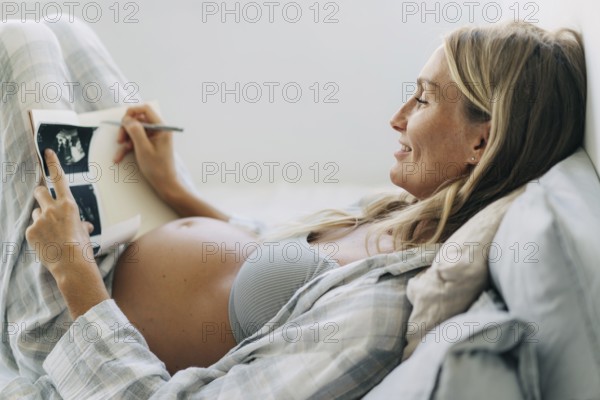 Eine schwangere Frau macht sich in einem Notizbuch Notizen über das Ultraschallergebnis