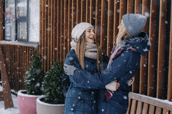 Erwachsene Freundinnen, die sich umarmen und lachen und sich über das verschneite, kalte Wetter freuen