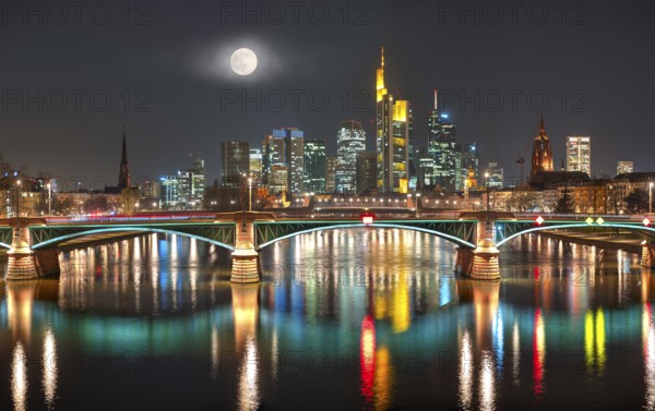 The illuminated skyline of the city centre of Frankfurt am Main at night and full moon with the river Main in the foreground, Frankfurt am Main, Germany