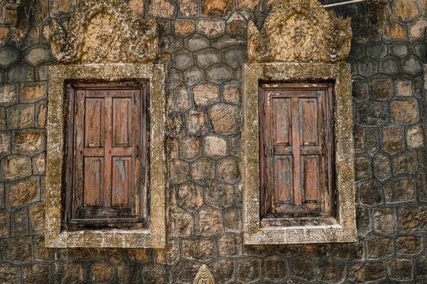 Twin weathered windows set in a rustic stone wall, suggesting an old and textured appearance