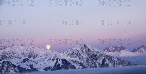 full moon rising into a pink sky in a winter mountain landscape in the Alps of Switzerland