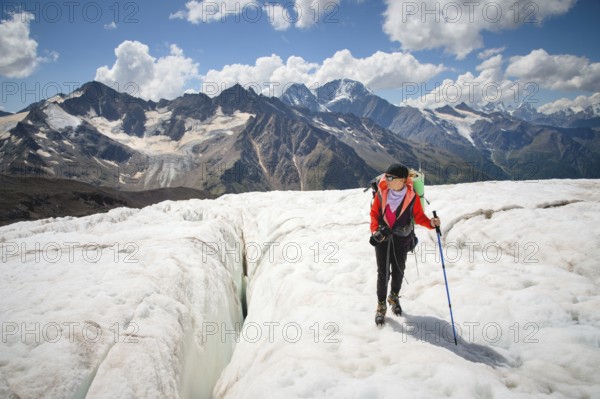 Female mountaineer enjoying the beauty of the glacier walks on the glacier in the crampon and sunglasses. Against the backdrop of the high mountains of the Caucasus sky and clouds