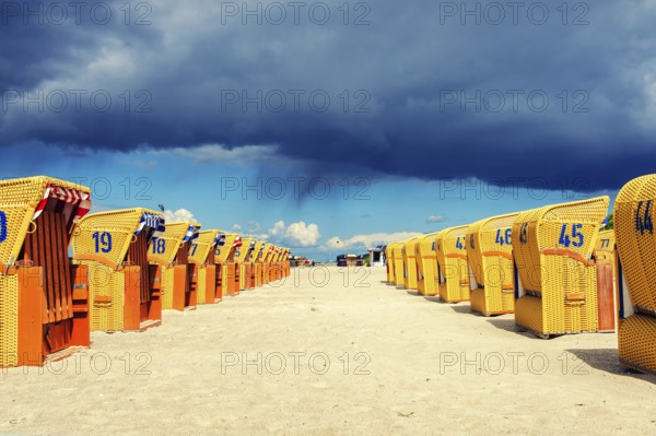 Yellow beach chairs in two rows under dark rain clouds in the sunshine
