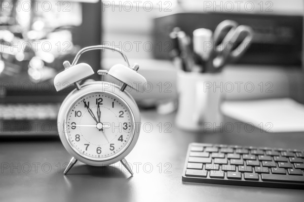 Alarm clock on the desk, office stuff in the blurry background, deadlines and todos