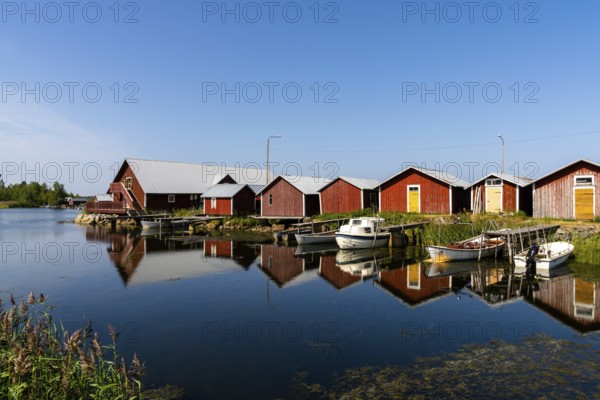 Svedjehamm, Finland - 28 July, 2021: colorful fishing cottages and boats reflected in the water under a blue sky