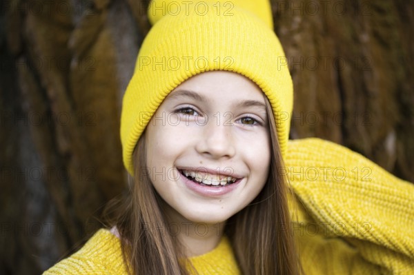 Cute and happy teenage girl with braces smiling at camera in yellow clothes in park. Concept of dentist and orthodontist. Pretty teenage girl wearing teeth appliance smiling happily outdoors