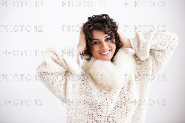 Pretty young girl with dark curly hair and make-up in peacock colours wears a white jumper