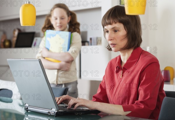 Mother and teenager girl with laptop computer together at home, Belgium