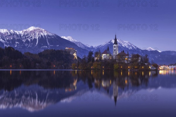 Scenic view of lake Bled at winter night with castle rock and St Martin church under beautiful starry sky reflected in lake water