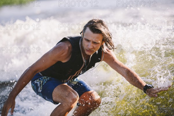 Active wakesurfer jumping on wake board down the river waves. Surfer on wave. Male athlete training on wakesurf training. Active water sports in open air on board. A man catches a wave on surf