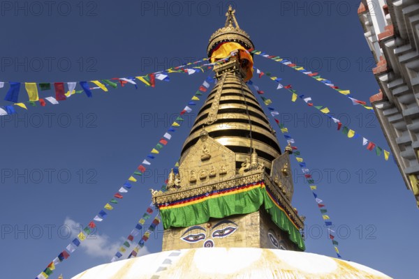 Swayambhunath, Swayambhu Mahachaitya, sometimes called the Monkey Temple, the Swayambhu stupa, one of the UNESCO World Heritage Sites of the Kathmandu Valley photographed in winter with the blue sky in the background. On the white dome stands a cubic part, the harmika, with eyes painted on its four sides, known as Eyes of Buddha or Wisdom Eyes. The golden spire is above it, and Buddhist prayer flags hang from the top. Kathmandu Metropolitan City, Bagmati Province, Nepal