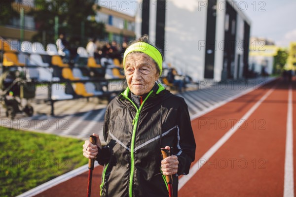 Active rest of the elderly theme. Sports and health in retirement. Caucasian very old woman with deep wrinkles doing Nordic walking exercises with sticks outside in the city stadium