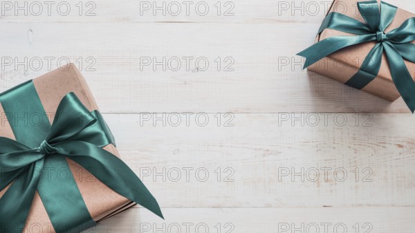 Two gift boxes in craft wrapping paper and green satin ribbon on white wooden table, copy space in center. Beautiful Christmas, New Year or Birthday presents, flat lay or top view. Banner